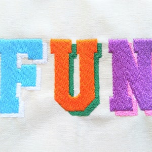 May include: Embroidered word "FUN" in colorful letters. The "F" is light blue with a white outline, the "U" is orange with a green outline, the "N" is purple with a pink outline.