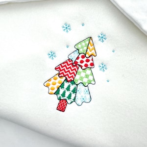 May include: White fabric with an embroidered Christmas tree design. The tree is composed of colorful, patterned sections in red, green, yellow, and blue, with snowflakes scattered around it. The design is on a white background.