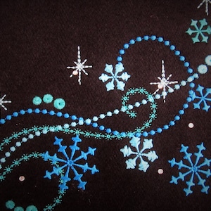 May include: A black fabric background with a design of blue and white snowflakes, stars, and swirls. The design is embroidered on the fabric.