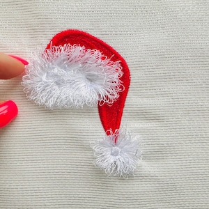 May include: A red and white embroidered Santa hat with a fluffy white pom-pom on a white fabric background.