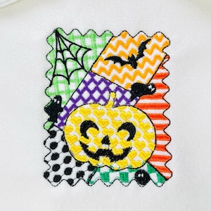 May include: Embroidered Halloween patch featuring a smiling yellow pumpkin, bats, spiders, and a spiderweb. The patch has a colourful patchwork design with a scalloped edge. The design includes green, orange, purple, and black elements.