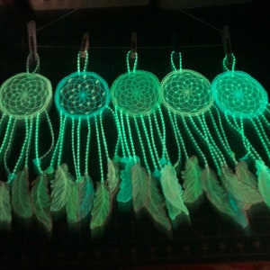 May include: Five green glow-in-the-dark dreamcatchers with feathers hanging from them.