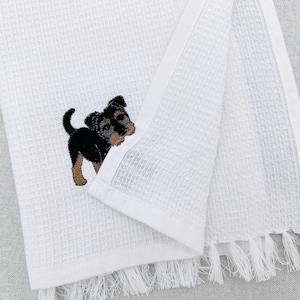 Peut inclure: Serviette de toilette blanche en nid d'abeille avec un motif brodé de chiot noir et beige. Le bord de la serviette est orné de franges. Le tissu est doux et absorbant, idéal pour une utilisation quotidienne.