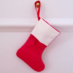 May include: A red and white Christmas stocking with a white cuff and a red body. The stocking is hanging from a gold hook.