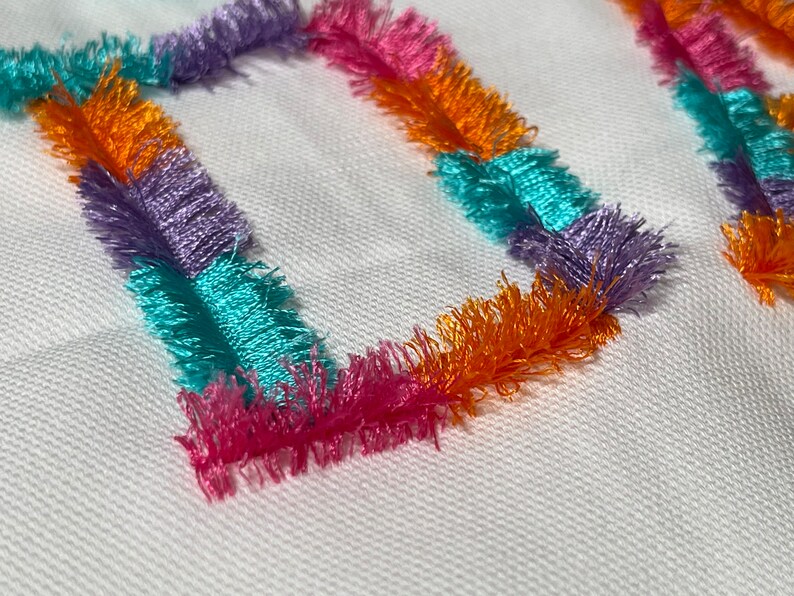 Peut inclure: Gros plan sur un tissu blanc avec deux carr&eacute;s color&eacute;s en tissu frang&eacute;. Les carr&eacute;s sont en tissu orange, rose, violet et turquoise.