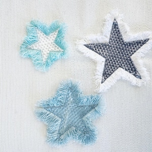 May include: Three decorative stars with fringed edges. One star is blue with white stitching, one is blue with blue stitching, and one is gray with white stitching.