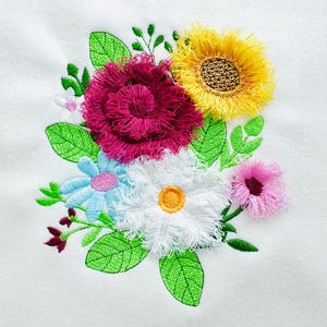 May include: Embroidered floral design featuring a cluster of colorful flowers. The arrangement includes a large, textured magenta rose, a yellow sunflower, and various other blooms in white, blue, and pink, with green leaves. The design is on a white background.