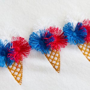 May include: Three embroidered ice cream cones with red, white, and blue frosting. The cones are stitched with a gold thread.