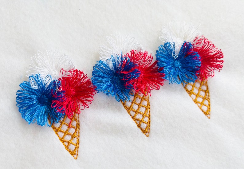 May include: Three embroidered ice cream cones with red, white, and blue frosting. The cones are stitched with a gold thread.