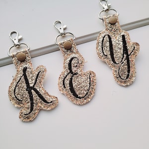 May include: Three gold glitter keychains with black embroidered letters K, E, and Y. Each keychain has a silver metal clasp.