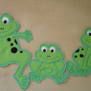 May include: Three green felt frog appliques with black eyes and black spots. The largest frog is jumping with its legs outstretched. The other two frogs are sitting with their legs tucked under them.