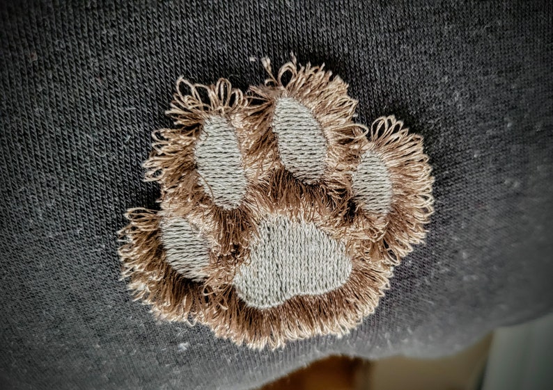 May include: A brown embroidered paw print on a dark gray fabric background.