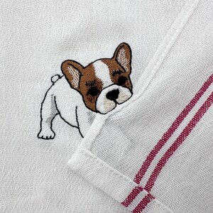K&ouml;nnte beinhalten: Wei&szlig;es Leinenhandtuch mit einem gestickten French Bulldog. Der Hund hat braune und wei&szlig;e Markierungen und ist schwarz umrandet. Das Handtuch hat zwei bordeauxfarbene Streifen und einen gefalteten Rand.