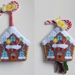 以下が含まれることがあります： キャンディーケーンとリボンがついたジンジャーブレッドハウス型のキーホルダー。家は白のフロスティングとカラフルなキャンディーの装飾が施された茶色です。キーホルダーにはドアに赤いハートがあり、下には鍵がぶら下がっています。