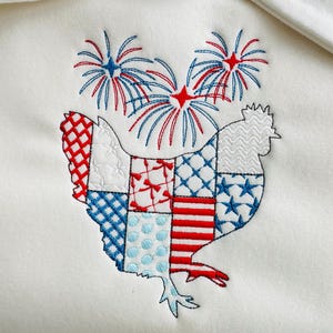 May include: A white fabric with an embroidered design of a rooster made of red, white, and blue patchwork squares. The rooster is standing under three red, white, and blue fireworks.