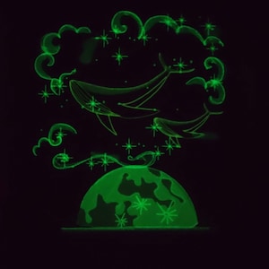 May include: A green glow-in-the-dark illustration of a whale jumping out of the ocean, with stars and clouds in the background. The whale is jumping over a green globe.