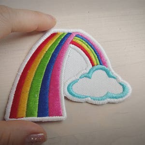 May include: A colourful rainbow patch with a white cloud, ideal for adding a whimsical touch to clothing, bags, or crafts.