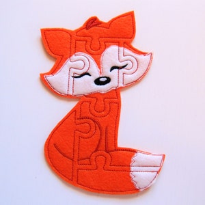 May include: Orange felt fox puzzle with white felt accents. The fox is sitting with its tail curled around its body. The puzzle is made up of multiple pieces that fit together.
