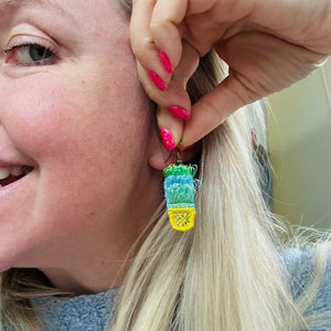 May include: A pair of colorful crocheted earrings in the shape of a cactus. The earrings are green, blue, and yellow.