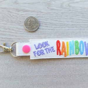 May include: White fabric keychain with a pink button and the text "Look for the Rainbow" embroidered in rainbow colors.