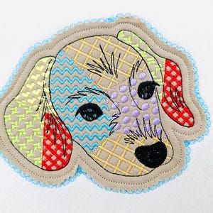 May include: Embroidered patch featuring a dog's head with a patchwork design. The dog's face has a tan background with sections of blue, yellow, green, red, and purple. The patch is outlined in a light blue scalloped edge.