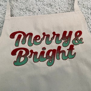 May include: A white apron with the text "Merry & Bright" embroidered in red and green.