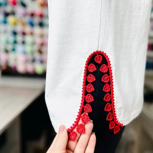 May include: White shirt with red heart-shaped trim along the bottom edge of the sleeves.
