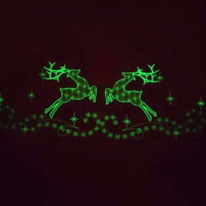 May include: Two green glowing reindeer silhouettes with antlers, jumping over a line of green glowing stars. The reindeer are facing each other and are in a dark background.