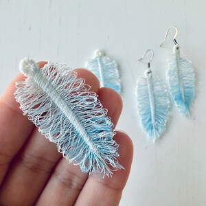 K&ouml;nnte beinhalten: Ein Paar blaue und wei&szlig;e Federn-Ohrringe. Die Ohrringe sind aus einem weichen, flauschigen Material gefertigt und haben einen zarten, femininen Look.