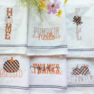 Pode incluir: Conjunto de seis toalhas de cozinha brancas com desenhos bordados em preto e laranja. Os desenhos incluem "Home", "Pumpkin Hello", "Fall", "Blessed", "Give Thanks" e "Thankful".