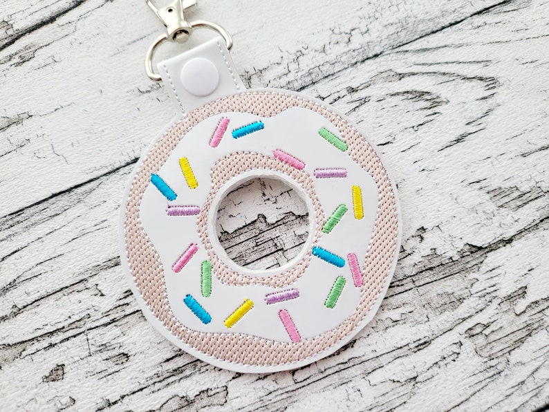 Pu&ograve; includere: Portachiavi a forma di ciambella bianca con glassa rosa e codette colorate. Il portachiavi ha un anello in metallo argentato.
