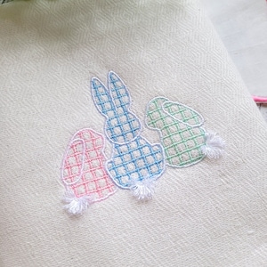 May include: A white kitchen towel with three embroidered bunnies. The bunnies are in pink, blue, and green gingham patterns.