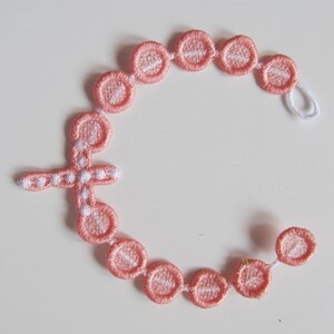May include: A pink and white beaded rosary with a cross charm. The beads are made of fabric and have a white embroidered design.