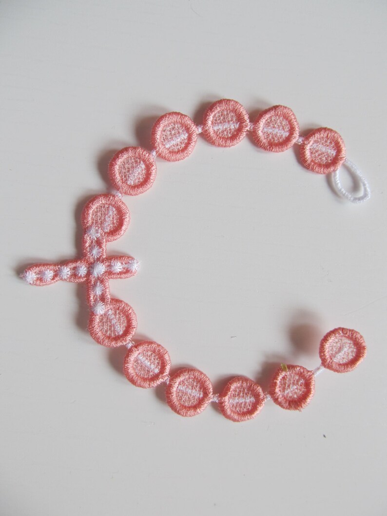 May include: A pink and white beaded rosary with a cross charm. The beads are made of fabric and have a white embroidered design.
