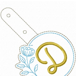 May include: A gold embroidered letter D with a blue floral design. The letter is surrounded by a blue circle and a gray circle.