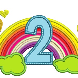 May include: A blue number two with a stitched outline is centered in front of a rainbow with yellow, orange, red, pink, purple, light blue, and white stripes.  Two green clouds are on either side of the number.  Three yellow hearts are scattered above the rainbow.