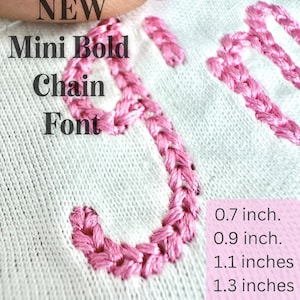 May include: Close-up of a white fabric with pink embroidered chain font letters. The text reads "NEW Mini Bold Chain Font." Measurements are listed in inches: 0.7, 0.9, 1.1, 1.3, 1.5, and 1.9 inches.