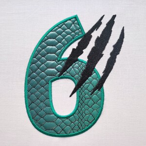 May include: A green number six with a snake skin pattern and black claw marks behind it.