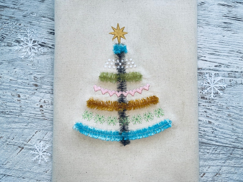 May include: A white fabric Christmas tree ornament with a gold star on top and colorful embroidery details.
