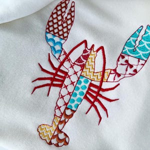 May include: An embroidered lobster with a patchwork design featuring blue, red, yellow, and white geometric patterns.