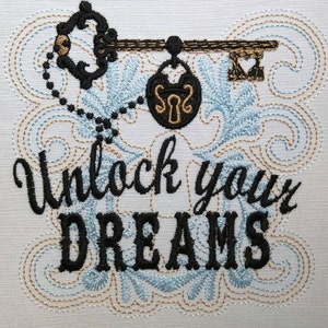 May include: Embroidered design featuring a vintage key with a padlock and the text "Unlock your DREAMS" in black thread on a white background.