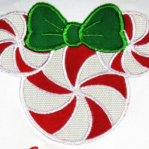 May include: Red and white candy cane shaped embroidery design with a green bow on top. The design is perfect for a Christmas themed project.