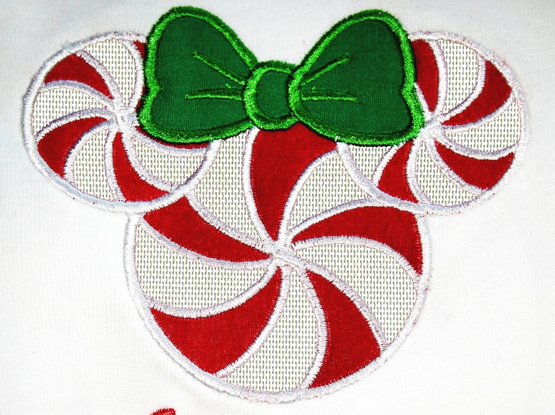 May include: Red and white candy cane shaped embroidery design with a green bow on top. The design is perfect for a Christmas themed project.