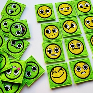Puede incluir: Un conjunto de 16 parches de fieltro verde con caras sonrientes amarillas bordadas, cada una con una expresión diferente. Los parches son perfectos para agregar un toque de fantasía a cualquier proyecto.