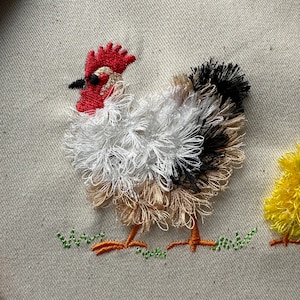 May include: Embroidered image of a white, brown, and black chicken with a red comb standing on green grass.
