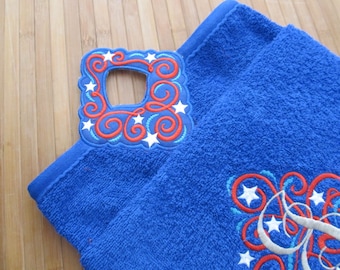 Puede incluir: Toalla de cocina azul con un diseño bordado en rojo, blanco y azul con estrellas y espirales. La toalla tiene un asa de bucle.