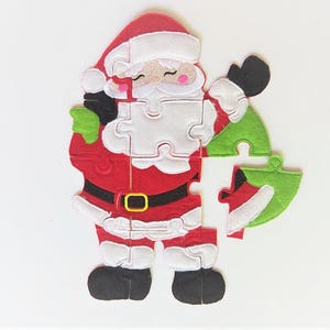 May include: A felt Christmas puzzle featuring Santa Claus with a red suit, white beard, and a green bag. The puzzle is made up of 10 pieces.