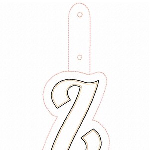 May include: A white letter Z with a gold outline, surrounded by a pink dashed line. The letter is attached to a pink loop.