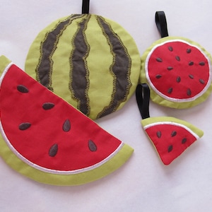 May include: A collection of watermelon-themed fabric items. Includes a whole watermelon, a slice, and two round pieces with a red interior and black seeds. The items are green, red, and brown with black hanging loops.