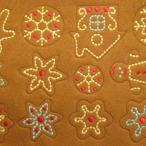 May include: A brown felt fabric with embroidered gingerbread cookies. The cookies are in the shapes of a gingerbread man, a star, a snowflake, a house, and a flower. The cookies are decorated with red, blue, and yellow thread.